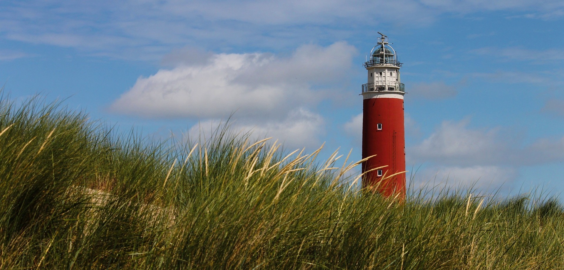 grüne Düne, blauer Himmel, roter Leuchtturm